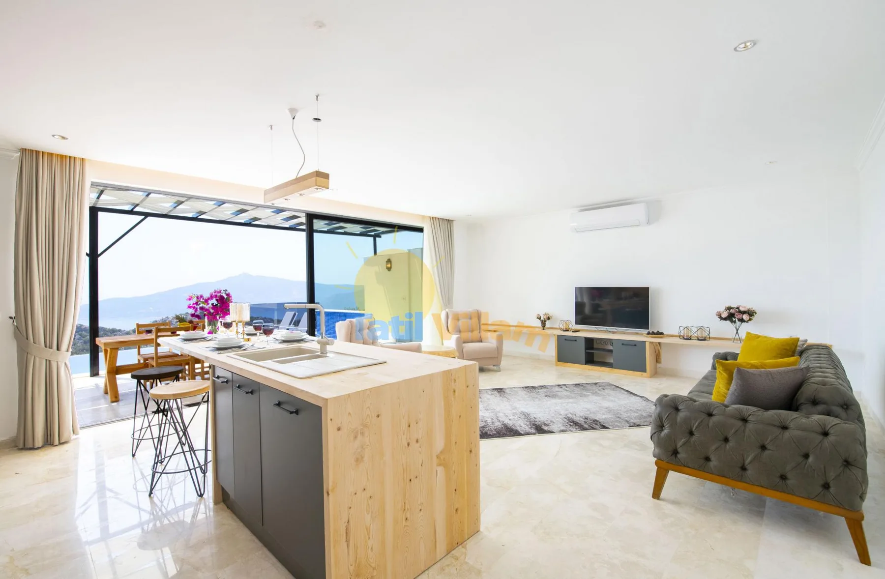 An open-plan living room and kitchen with large windows overlooking the outdoors.