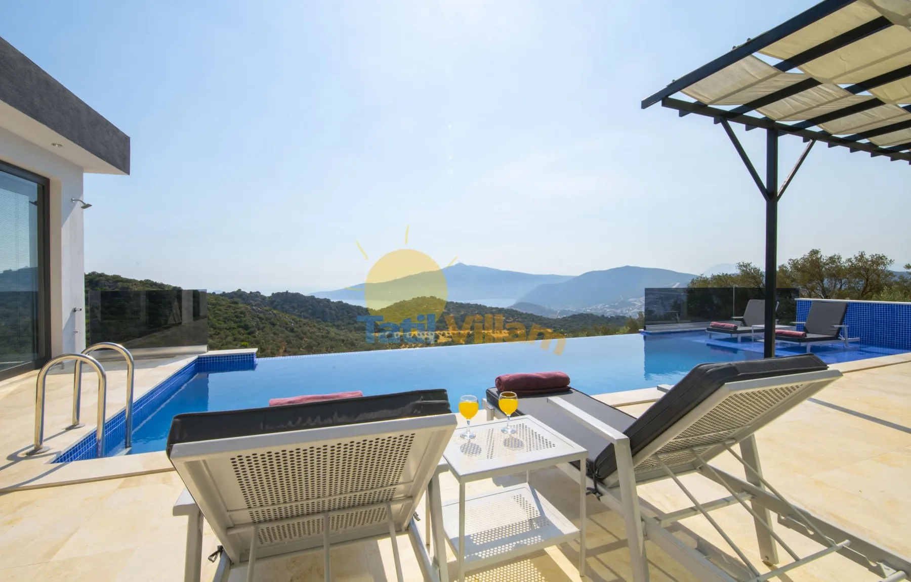 An outdoor pool with lounge seating overlooks a wooded mountain landscape.