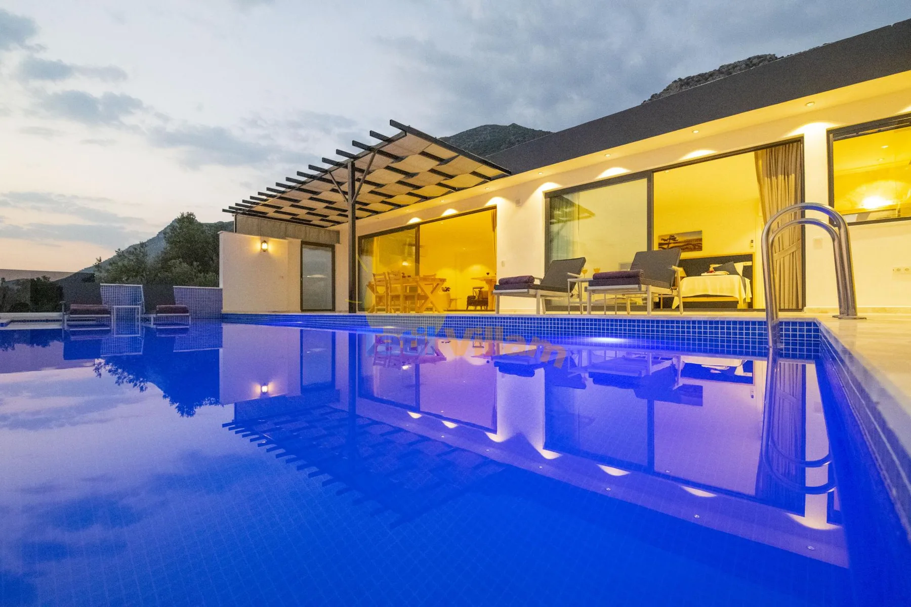 An illuminated swimming pool sits in front of a modern building at dusk.