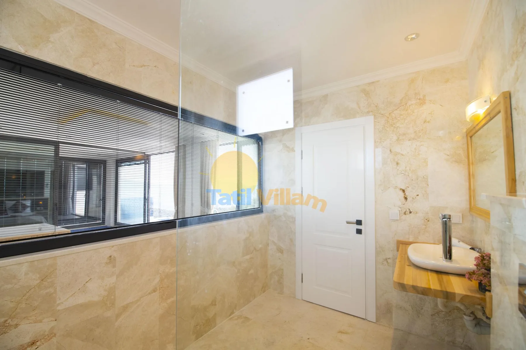 A tiled bathroom with a glass shower partition, white door, and wall-mounted sink.
