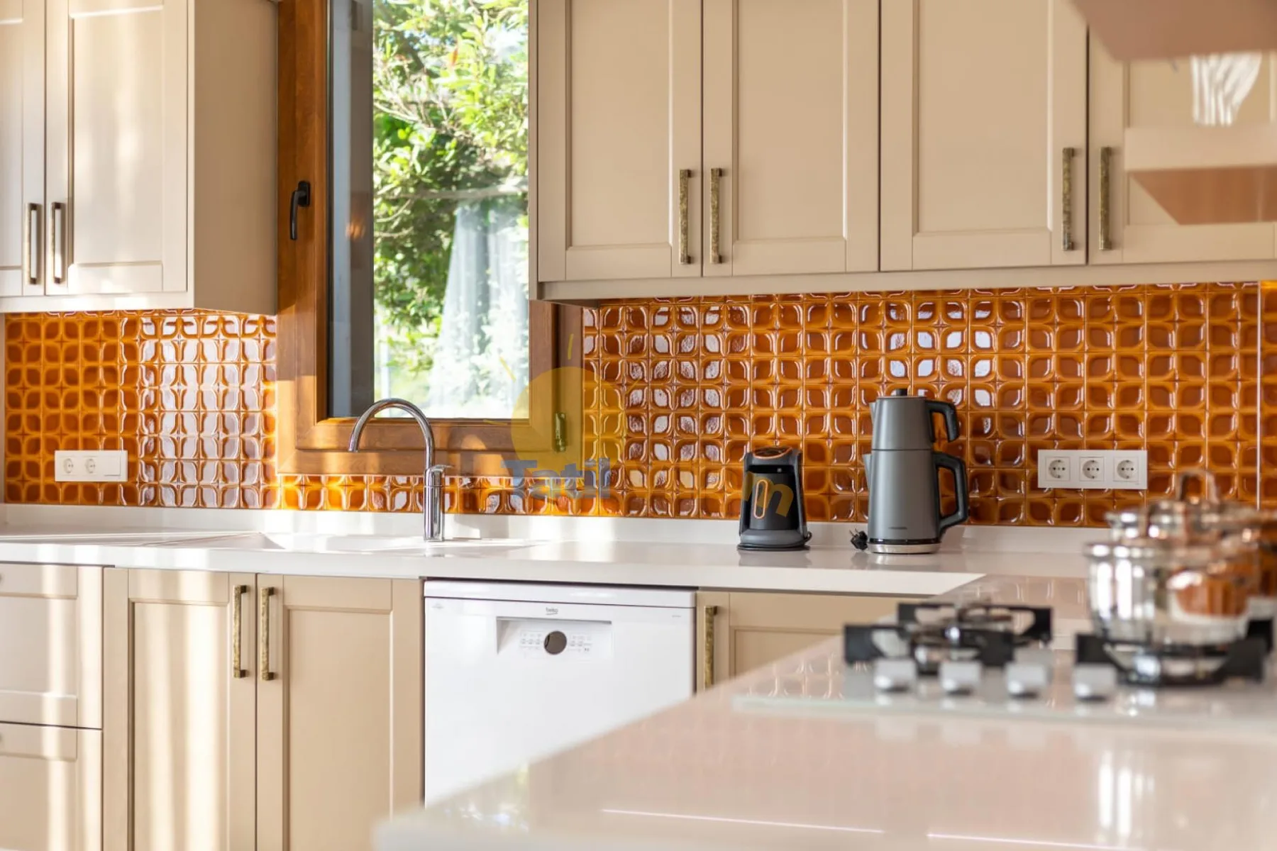 Una cocina luminosa con gabinetes claros, azulejos naranjas y una ventana sobre el fregadero.