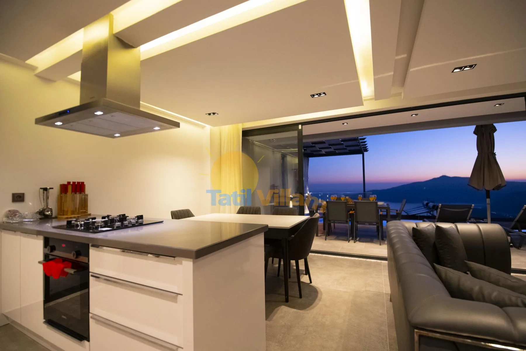 An open-plan kitchen and dining area with seating overlooking the sea at dusk.