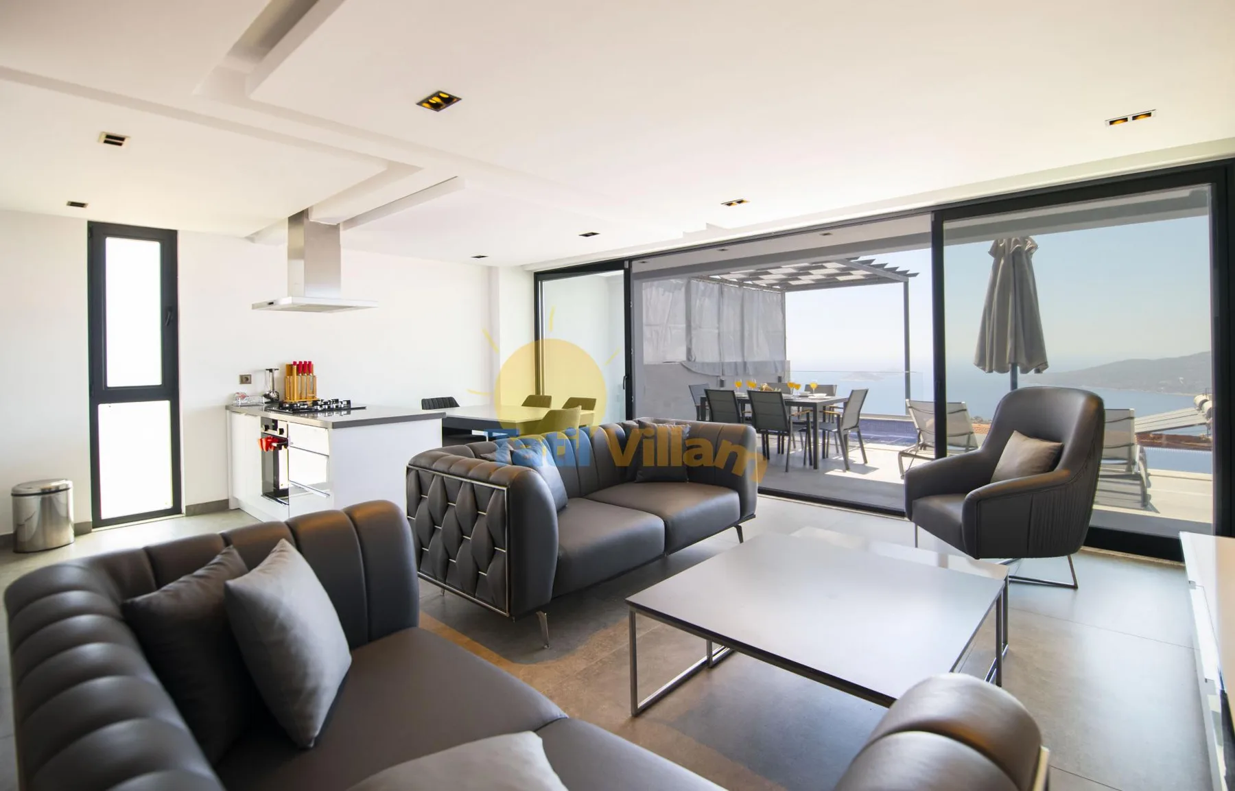 A bright open-plan living room and kitchen opens onto a terrace with outdoor seating.