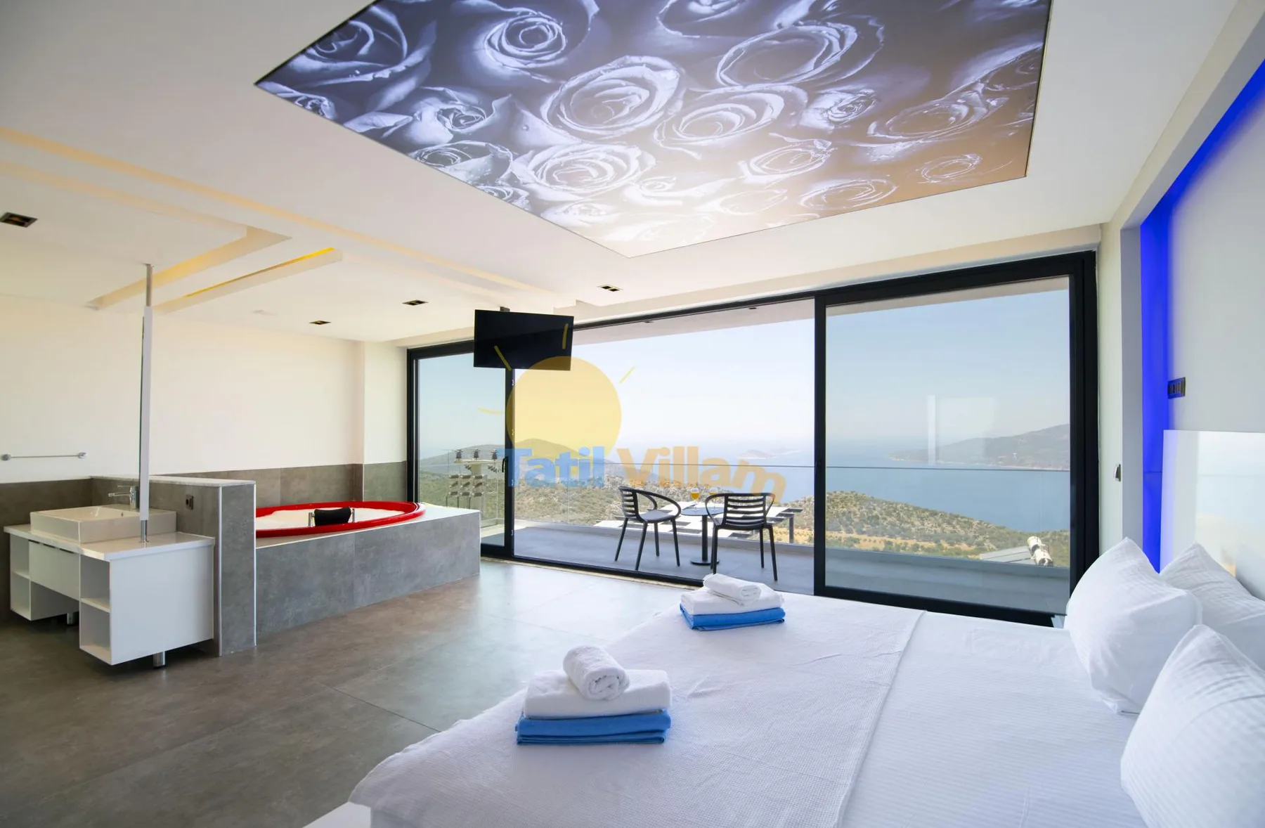 A bright bedroom opens onto a balcony with seating and a view of the sea.