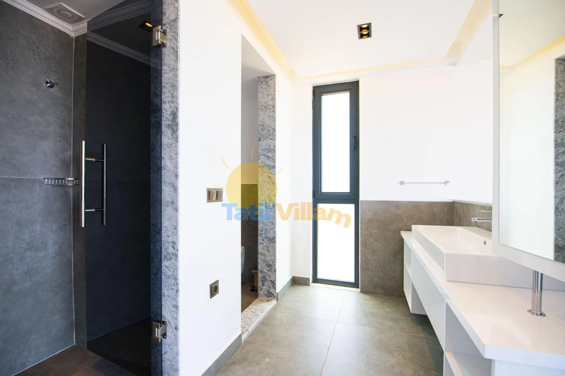 A bright bathroom with a shower area and a long white sink counter.