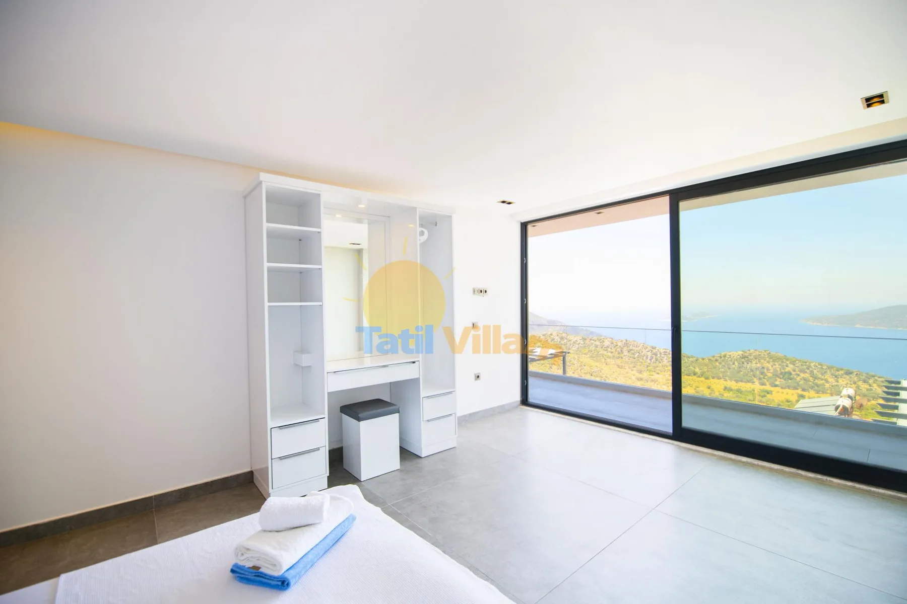A bright bedroom with built-in shelving and large windows overlooking the sea.