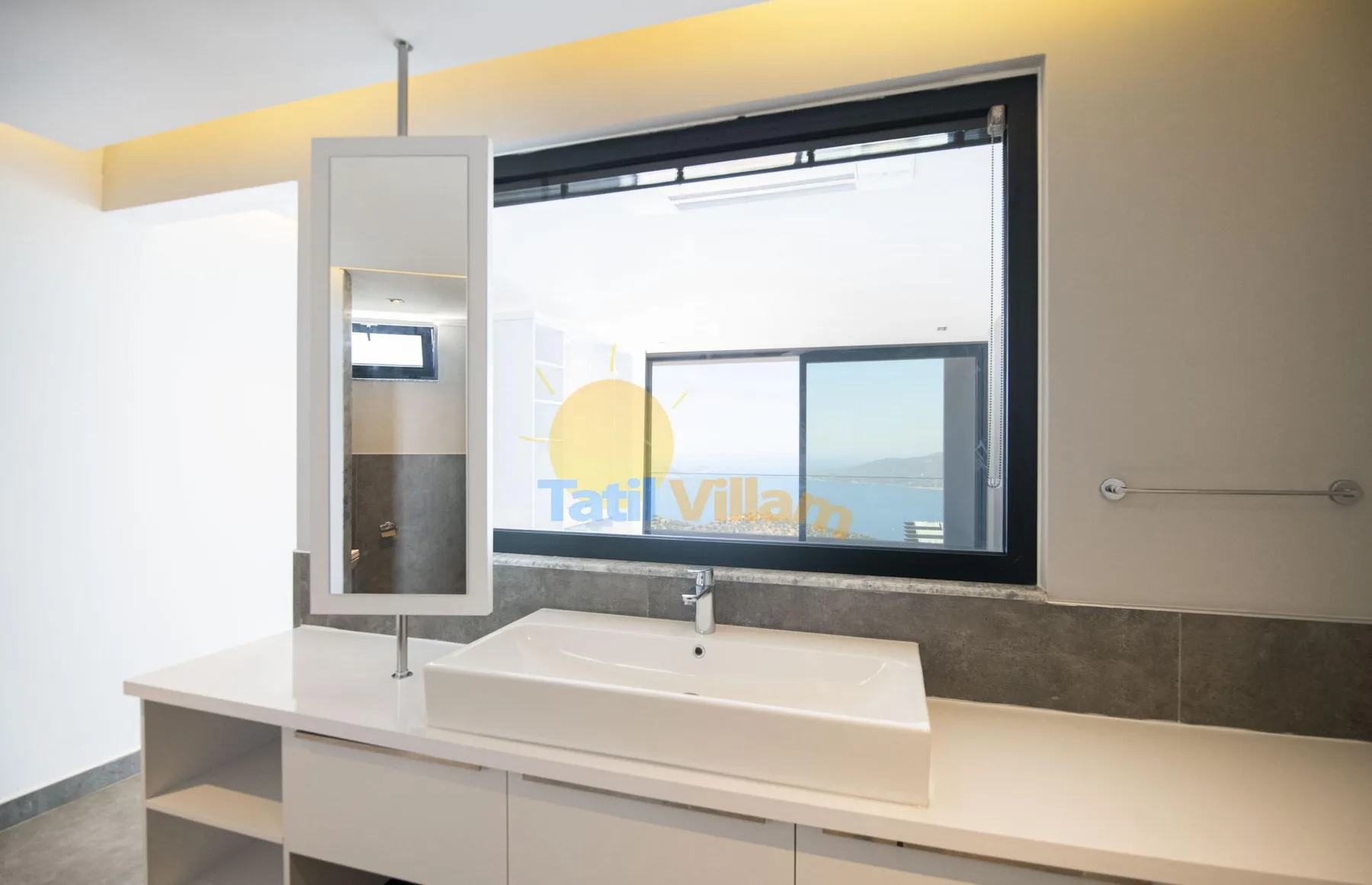A bathroom vanity with a sink sits beneath a large window.