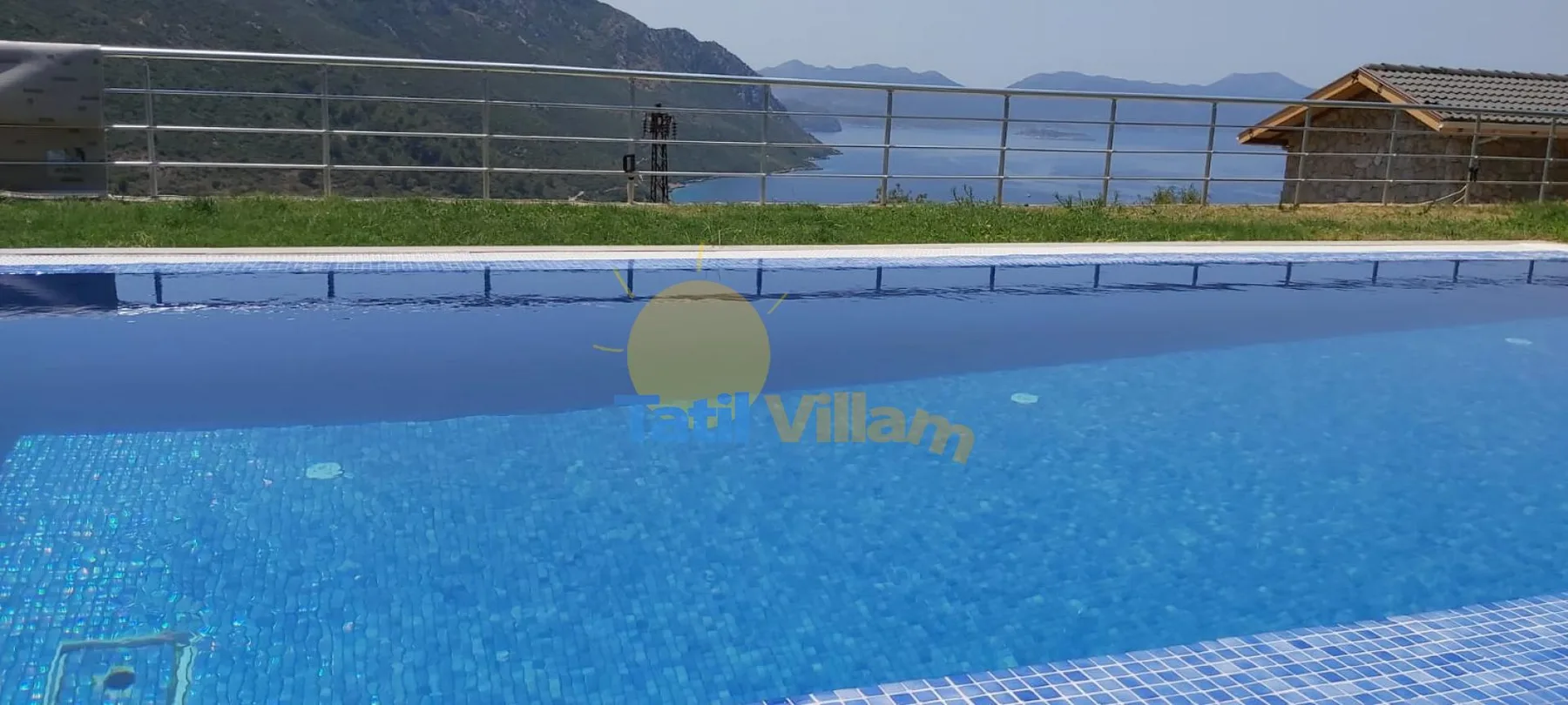 A blue swimming pool overlooks a body of water and distant hills.
