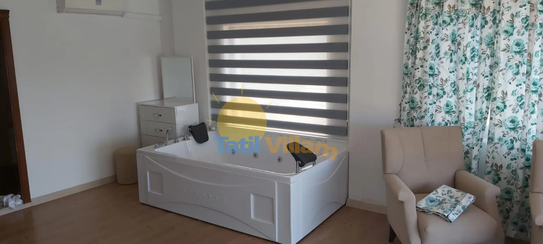 A bathroom features a large bathtub beside a cushioned seat and patterned curtains.