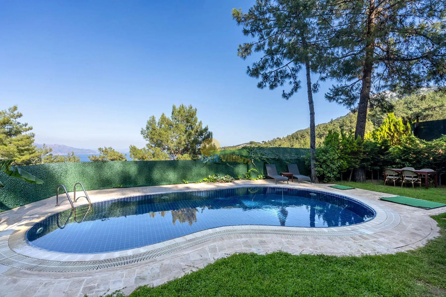 Una piscina al aire libre está junto a un césped, árboles y vistas a las montañas.