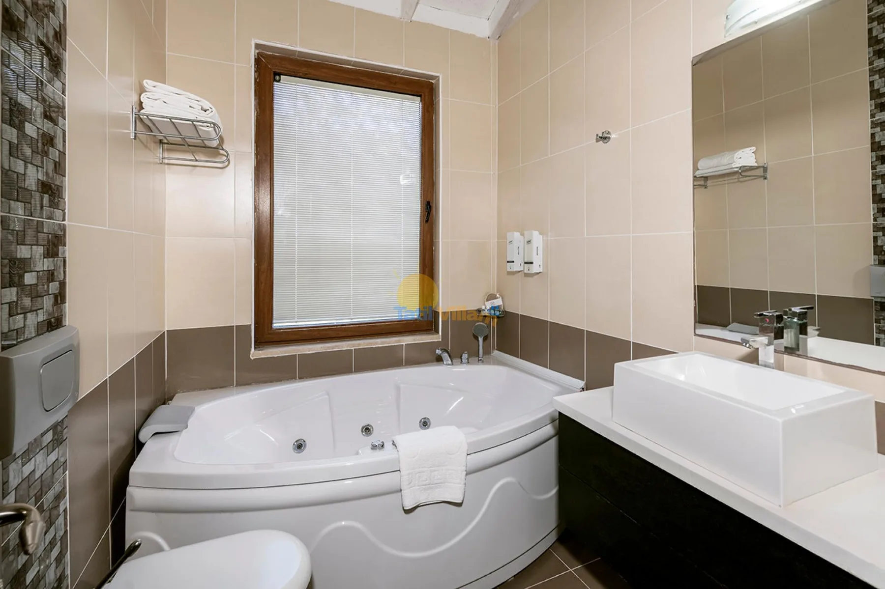 Un baño alicatado con una bañera en esquina y un lavabo bajo un espejo grande.