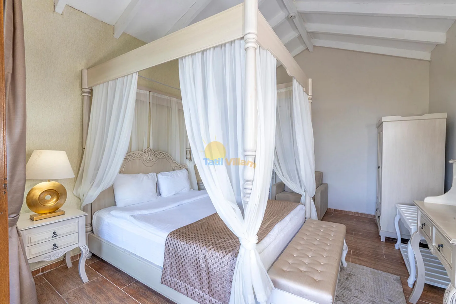 Un dormitorio con cama con dosel, cortinas blancas y un banco acolchado.