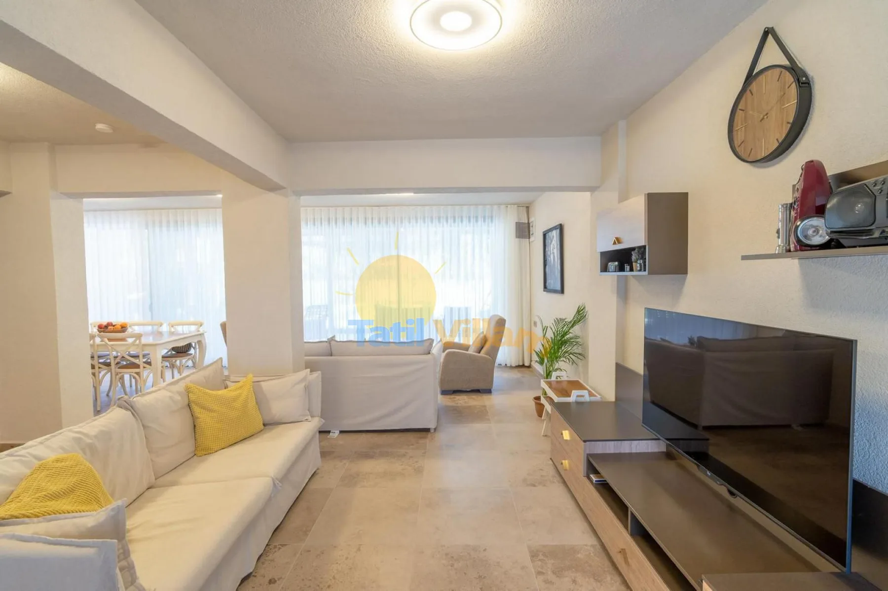 Una sala luminosa con asientos, un televisor y ventanales.