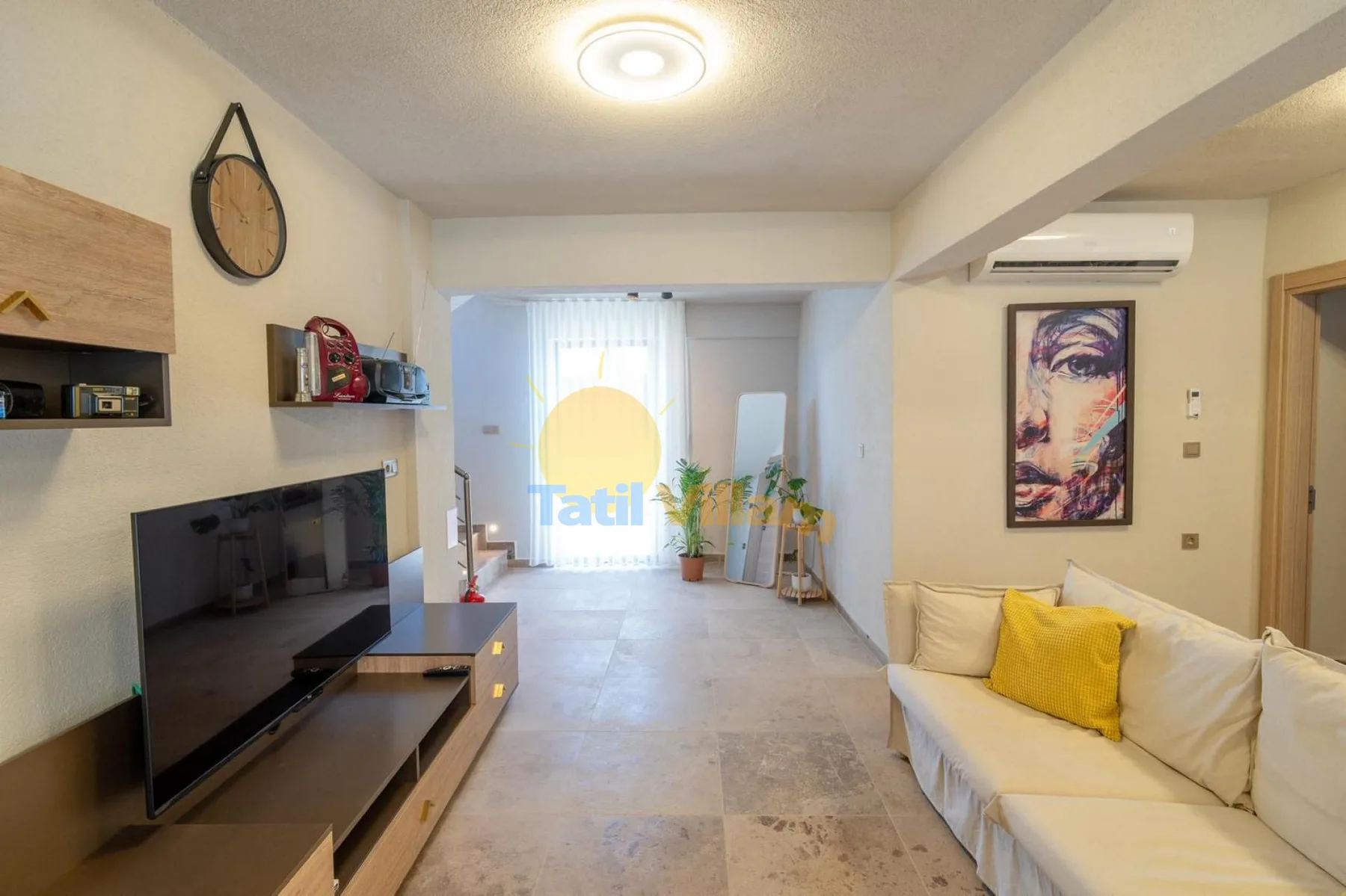 Una sala de estar con televisor, asientos y una ventana luminosa al fondo.
