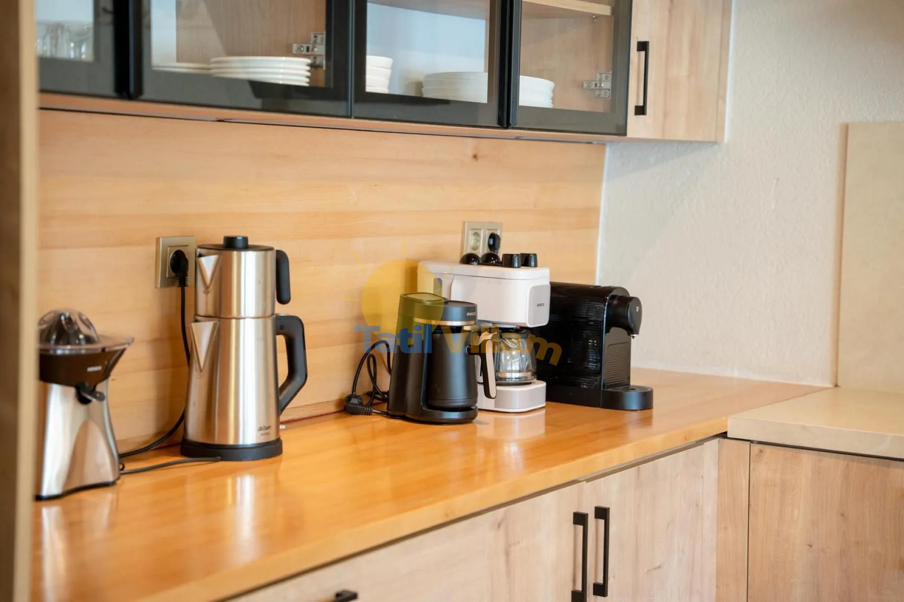 Una encimera de cocina con una tetera y aparatos para preparar café bajo los armarios.