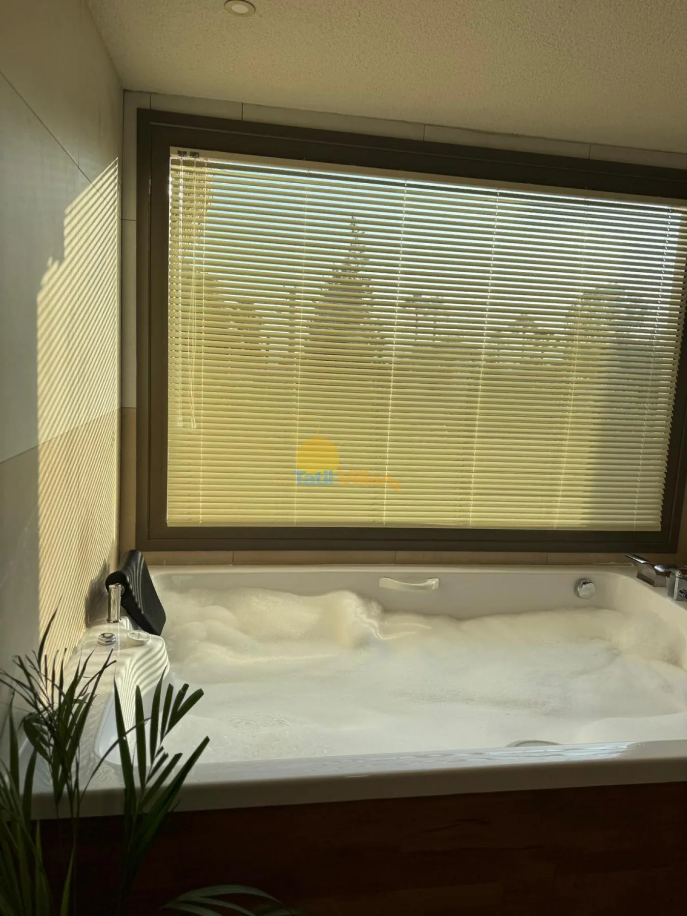 Una bañera amplia está debajo de una ventana con persianas cerradas.