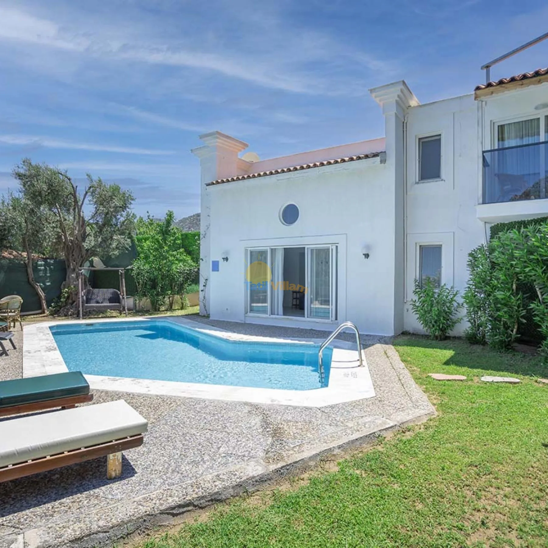Una piscina está junto a una casa blanca y un patio con césped.