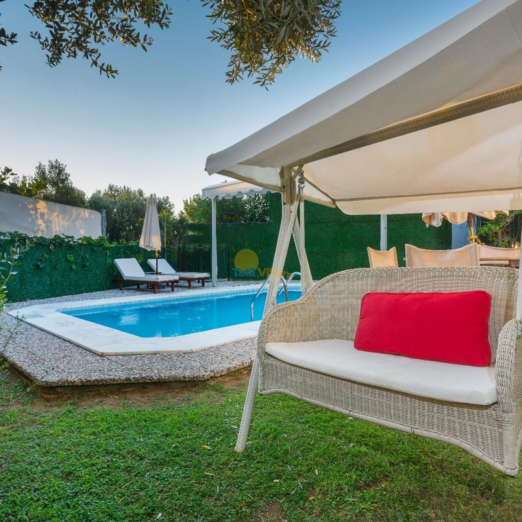 Una piscina en el jardín junto a asientos al aire libre bajo una gran cubierta de sombra.