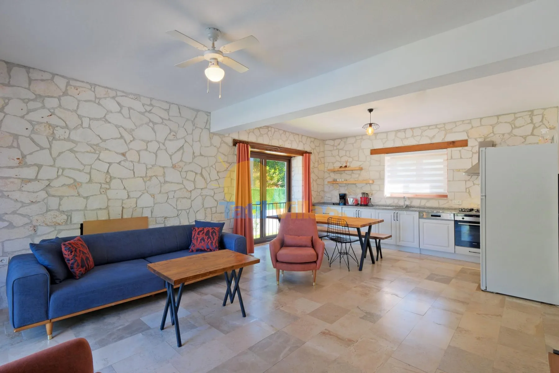 Una zona abierta de sala y cocina tiene paredes de piedra, asientos azules y una mesa de comedor.