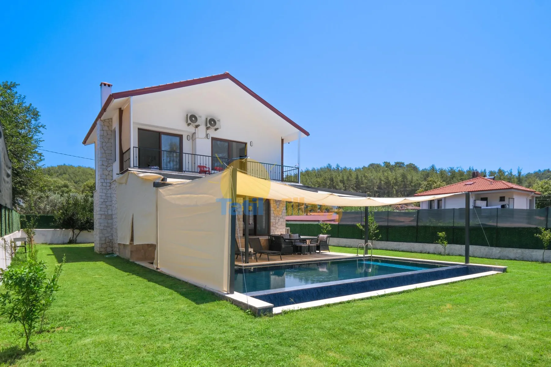 Una casa da a una piscina rectangular y un césped verde bajo una cubierta de sombra.