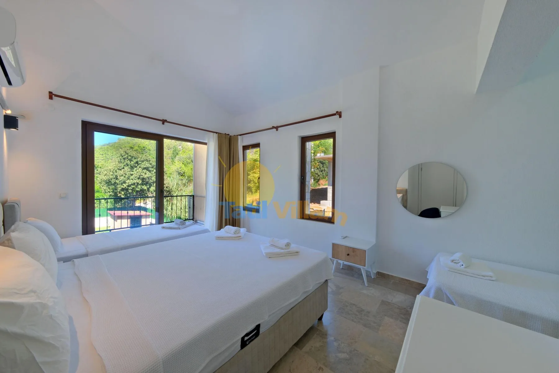 Un dormitorio luminoso con una cama grande junto a ventanas con vistas a la vegetación.