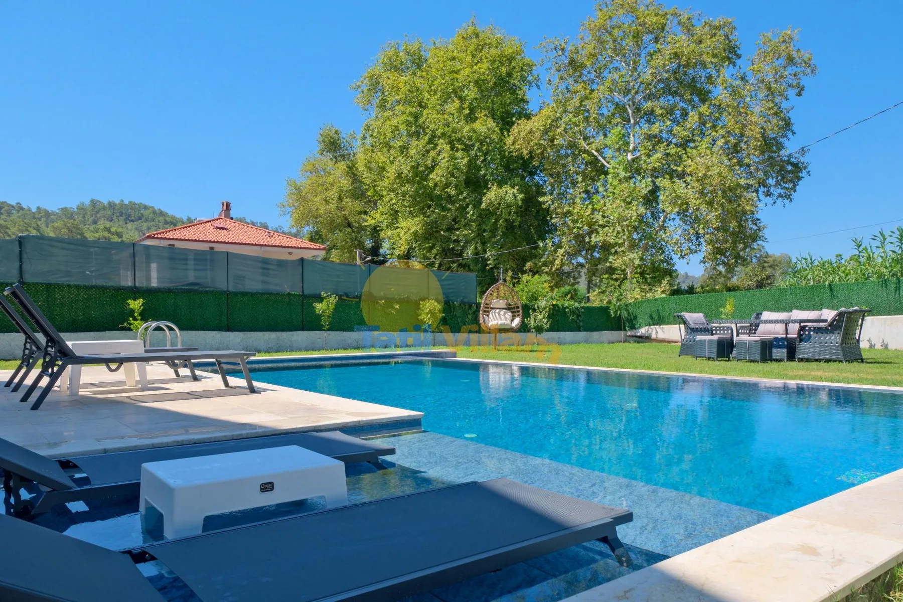 Una piscina al aire libre con asientos para descansar y árboles al fondo.