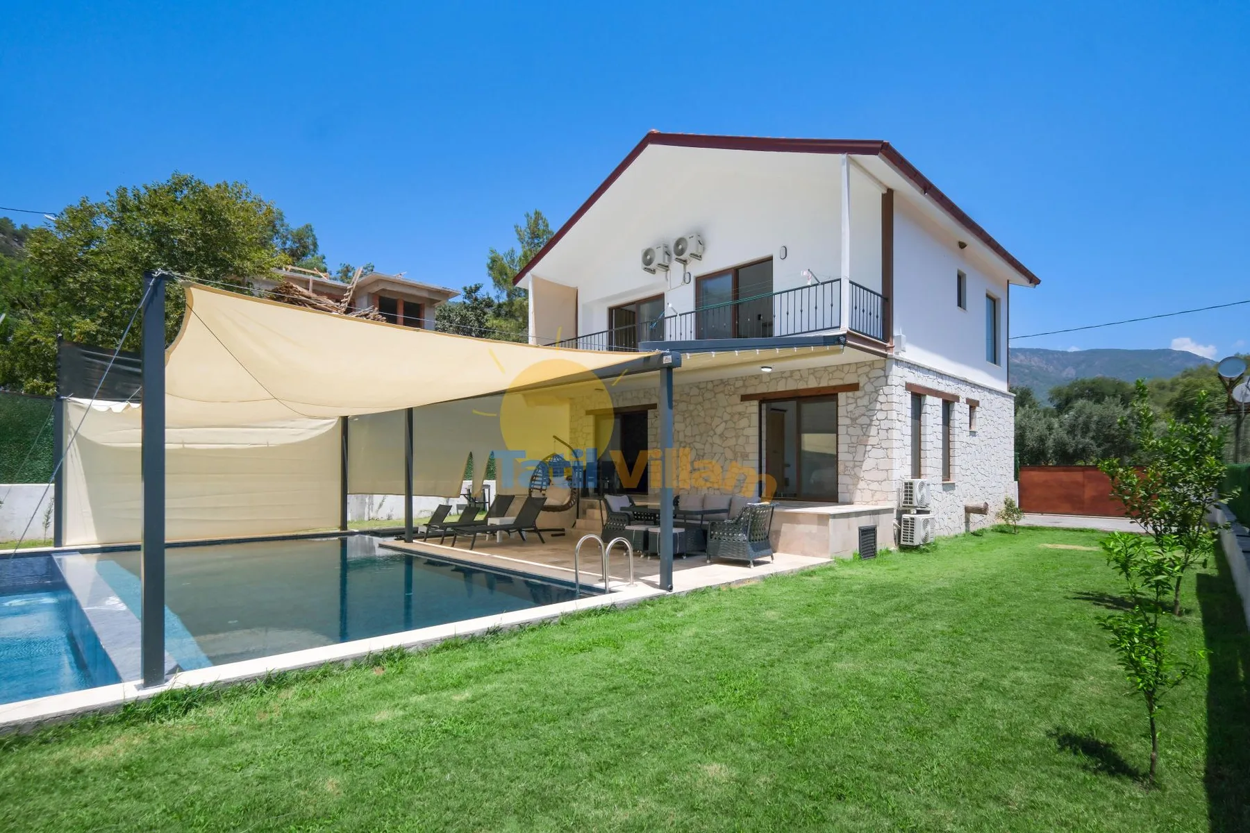 Una casa de dos pisos está junto a una piscina, con césped al frente.