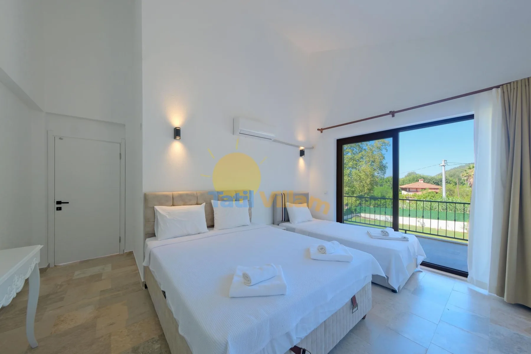 Un dormitorio luminoso con dos camas, ropa de cama blanca y una gran ventana con vistas a la vegetación.