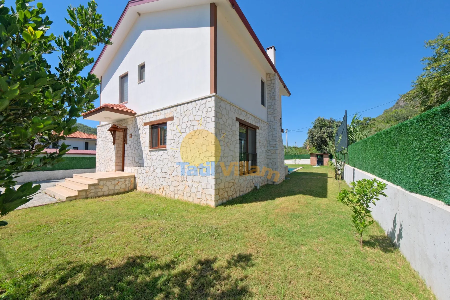 Una casa de dos plantas con la planta baja revestida de piedra está junto a un jardín con césped.