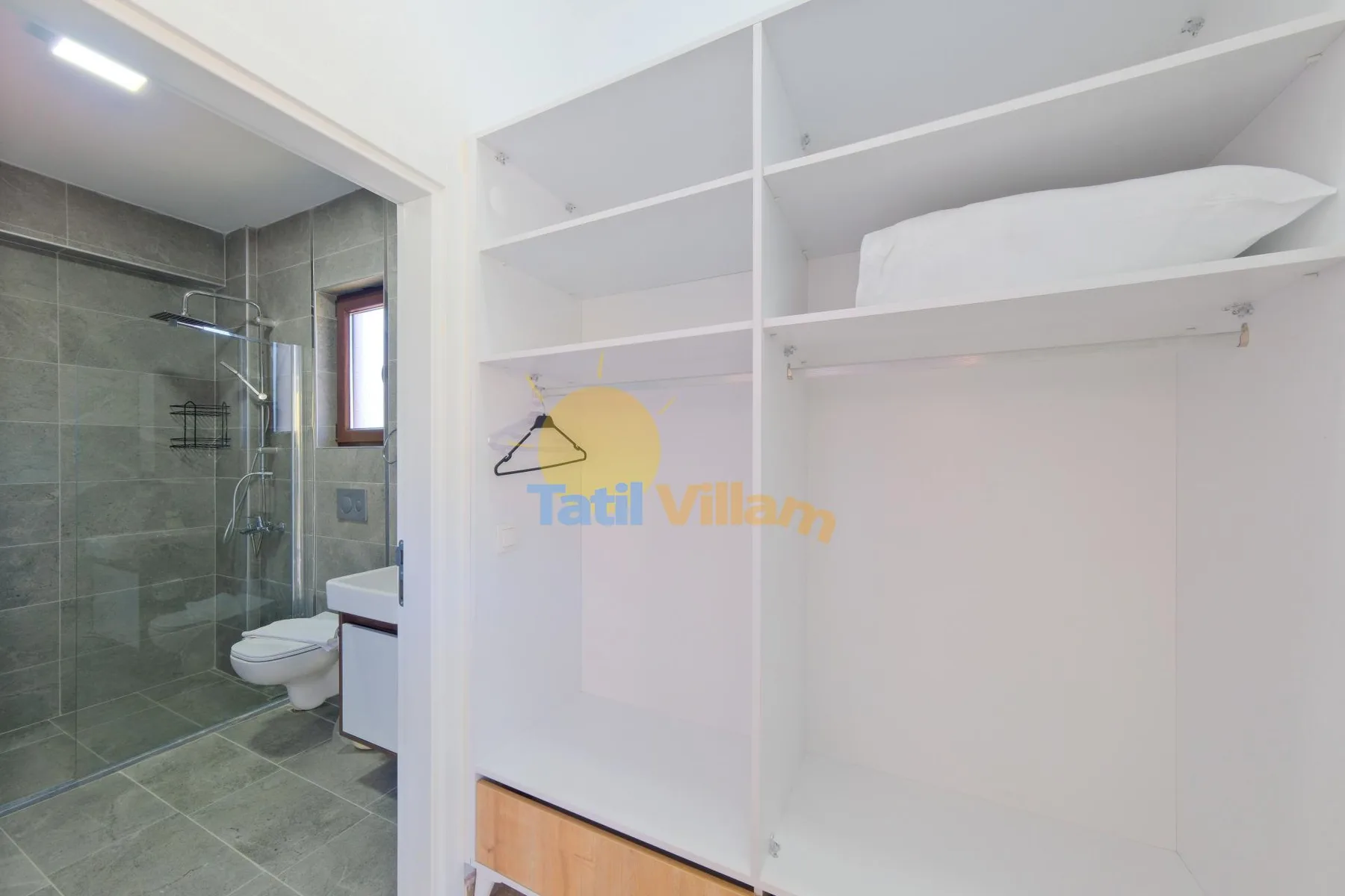 Un baño con una ducha de vidrio junto a estantes blancos abiertos y una toalla doblada.