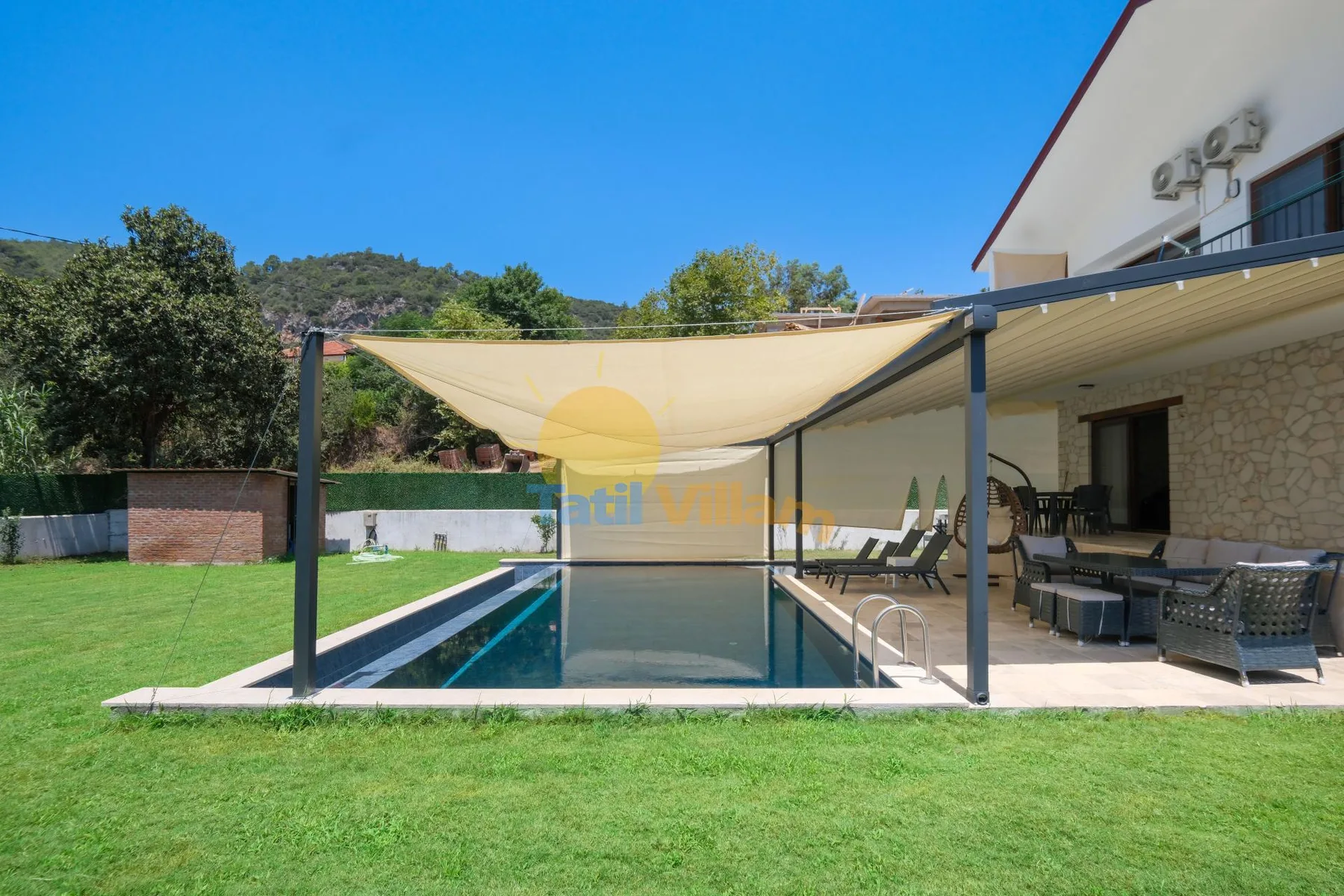 Una piscina y asientos de patio están bajo un toldo junto a la casa.