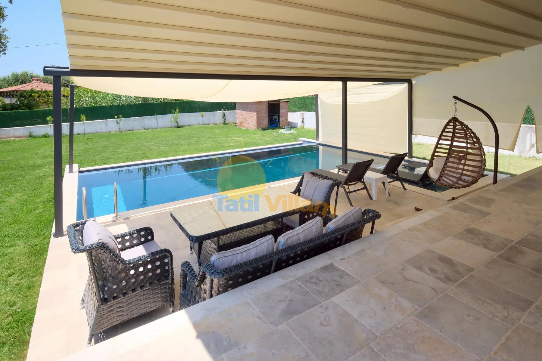 Un patio cubierto con asientos al aire libre da a una piscina y un césped.