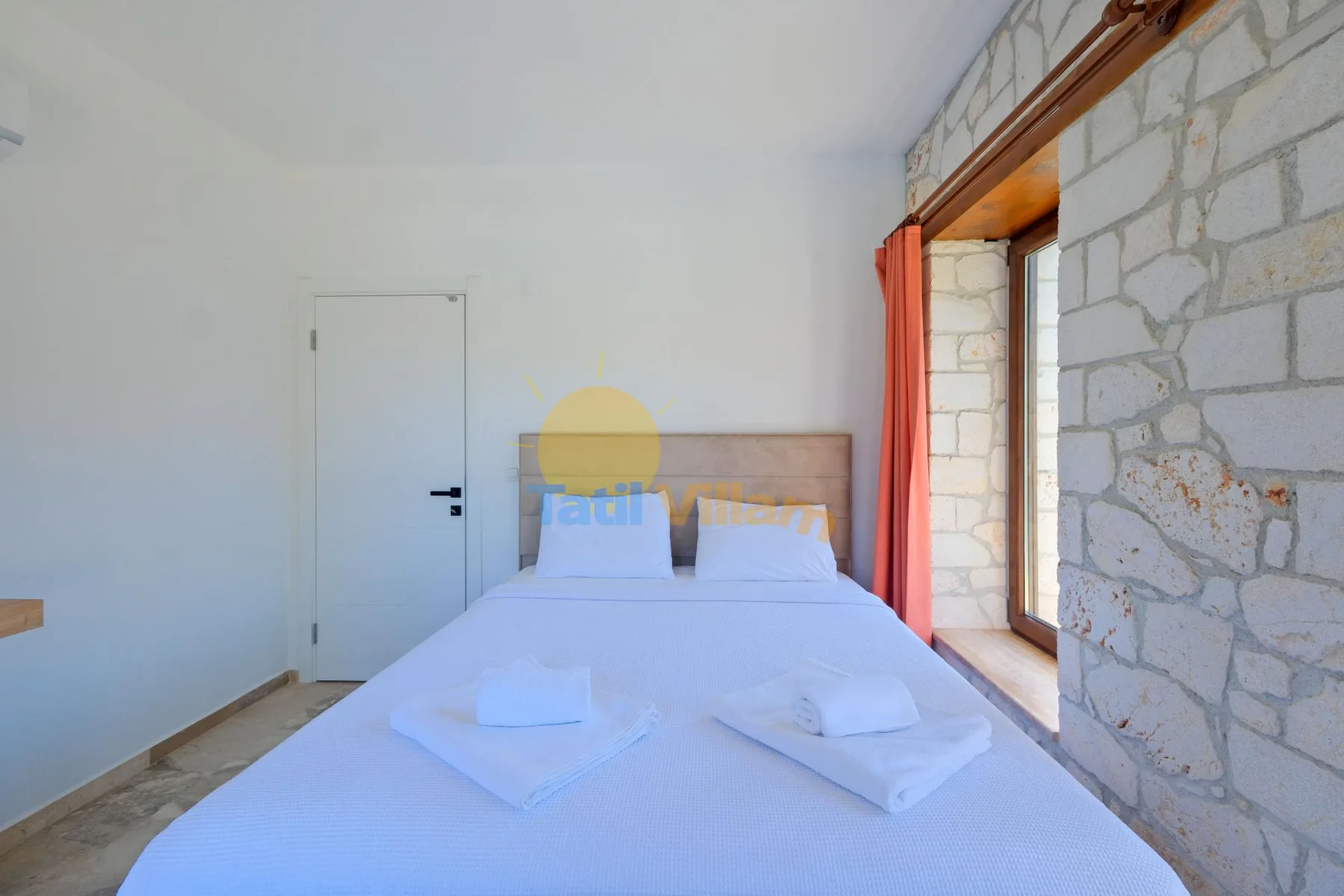 Un dormitorio con una cama tendida junto a una ventana alta y una pared de piedra.