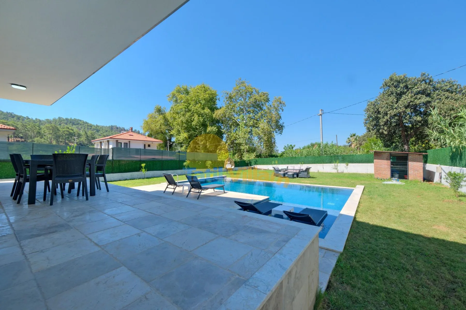 Un patio al aire libre con asientos da a una piscina y un césped.