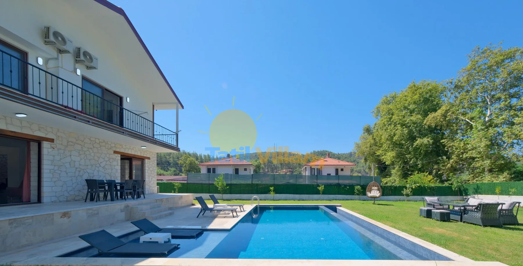Una piscina junto a una casa moderna, con tumbonas y césped verde.