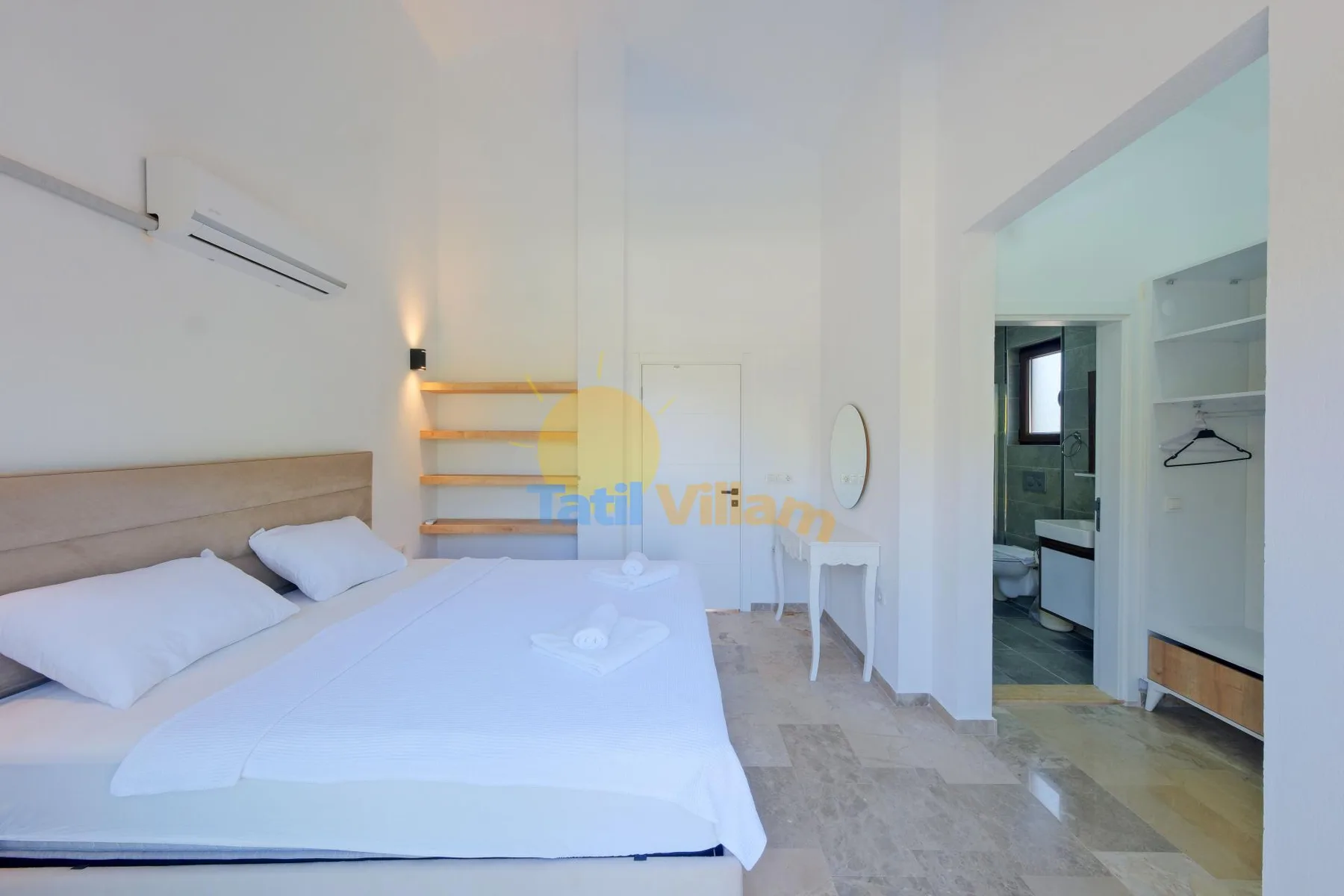 Un dormitorio luminoso con una cama, un escritorio pequeño y una puerta abierta al baño.