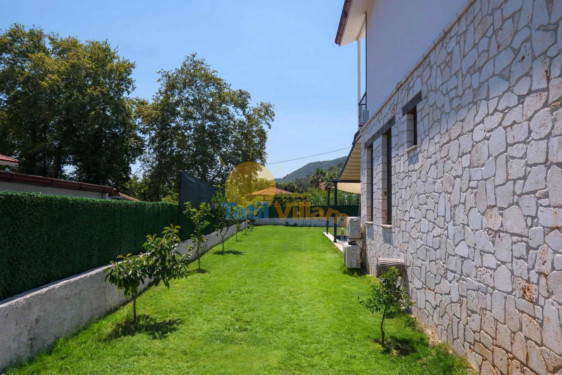 Un patio de césped se extiende junto a un edificio revestido de piedra y un seto alto.