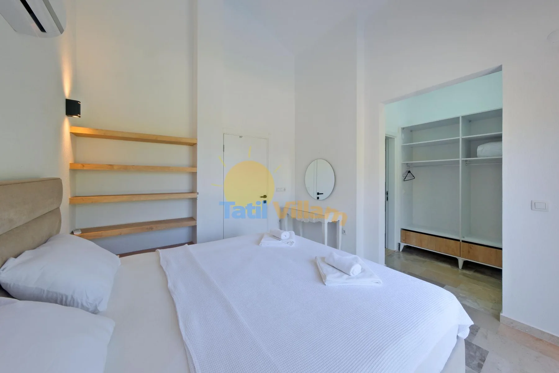 Un dormitorio luminoso con una cama bien hecha y estantes abiertos junto a la pared.