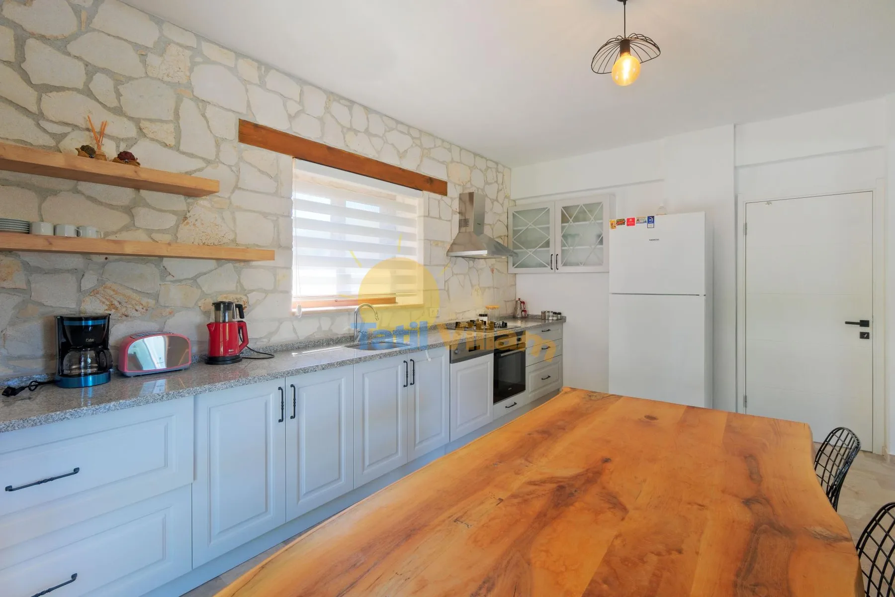 Una cocina luminosa con gabinetes blancos, una encimera y una mesa de madera.