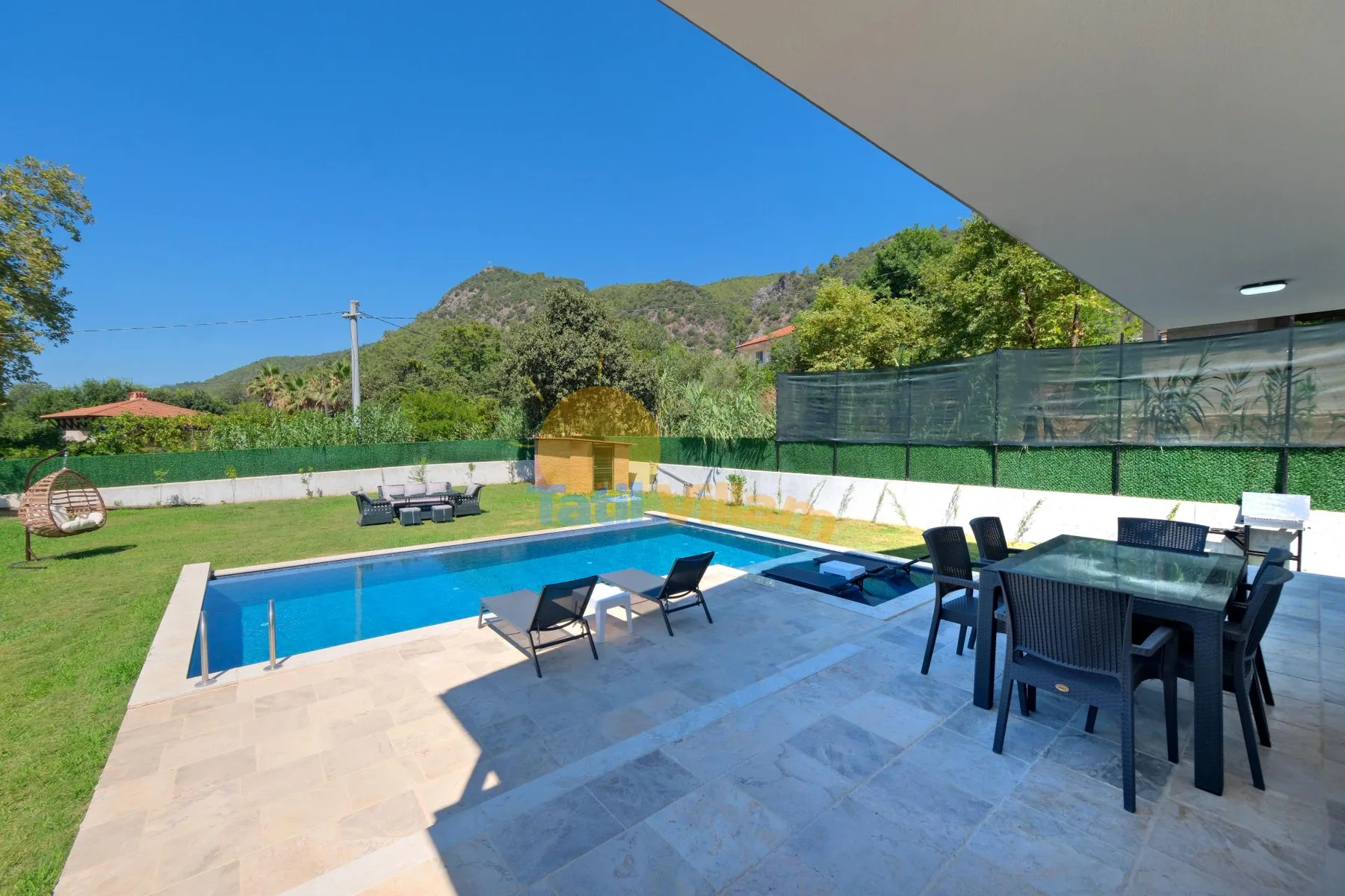 Una piscina al aire libre y asientos en el patio dan a un jardín con césped y colinas verdes.