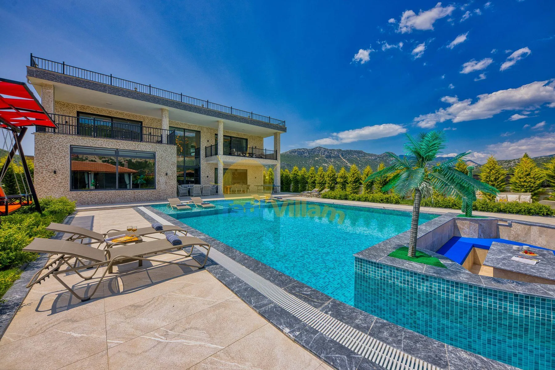 A modern building overlooks a swimming pool and surrounding mountain landscape.