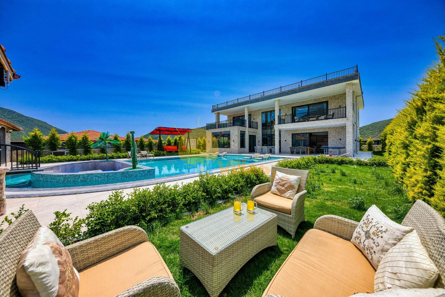 A modern house overlooks a swimming pool, with outdoor seating in the foreground.