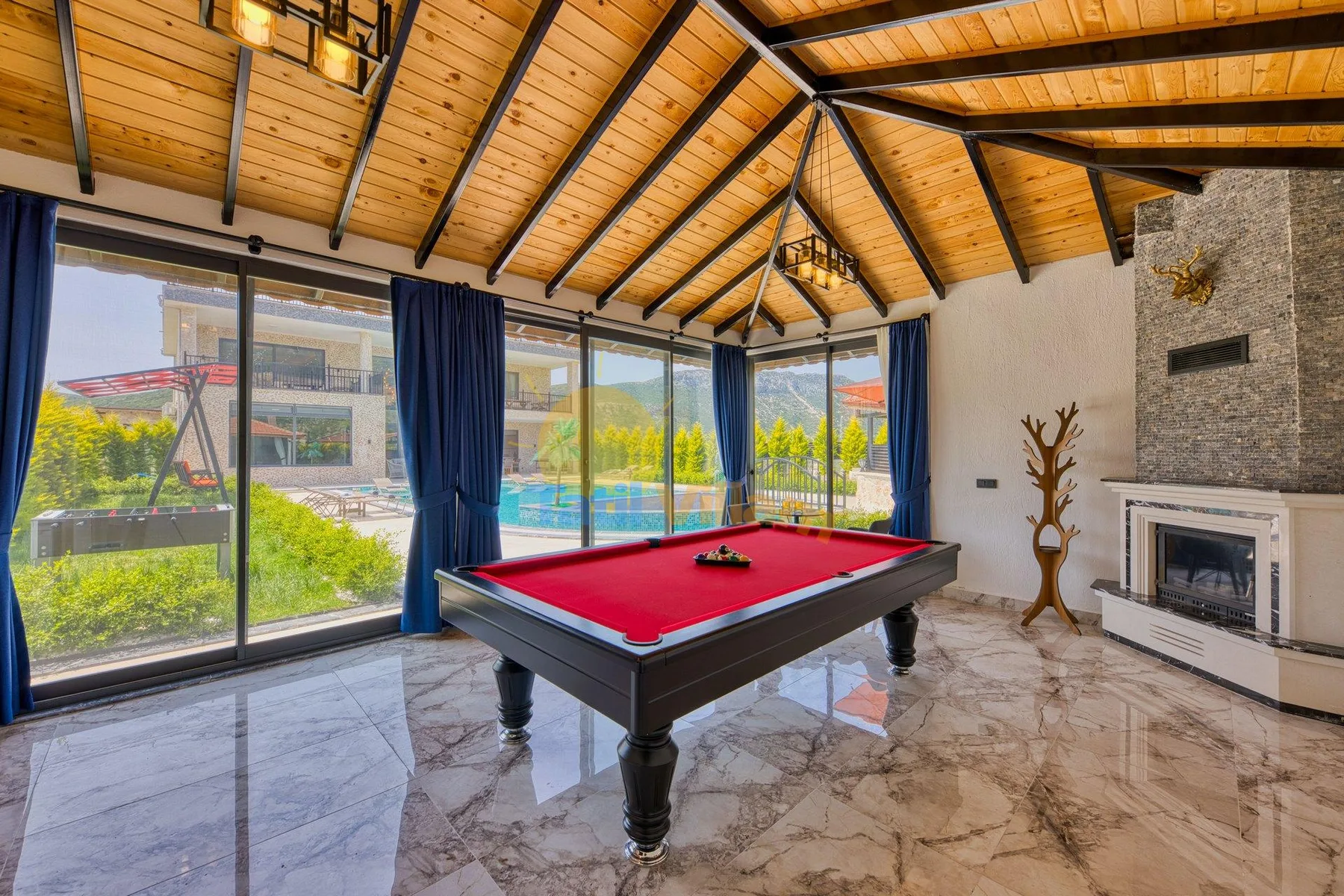 A game room with a red-felt billiards table beside large windows.