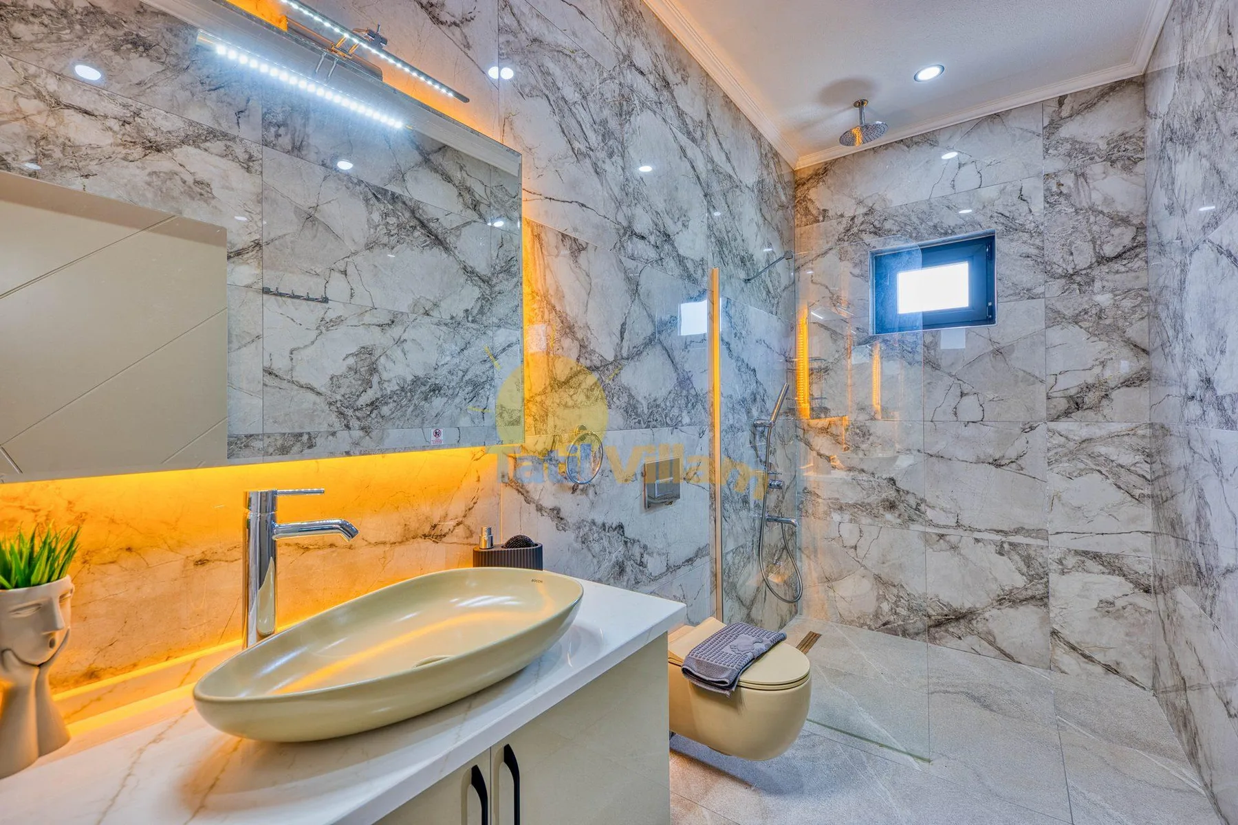 A marble-tiled bathroom with a sink, toilet, and glass shower partition.