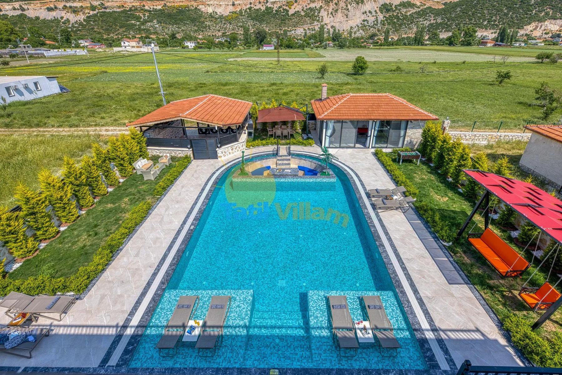 An outdoor swimming pool sits beside tiled walkways and low buildings.