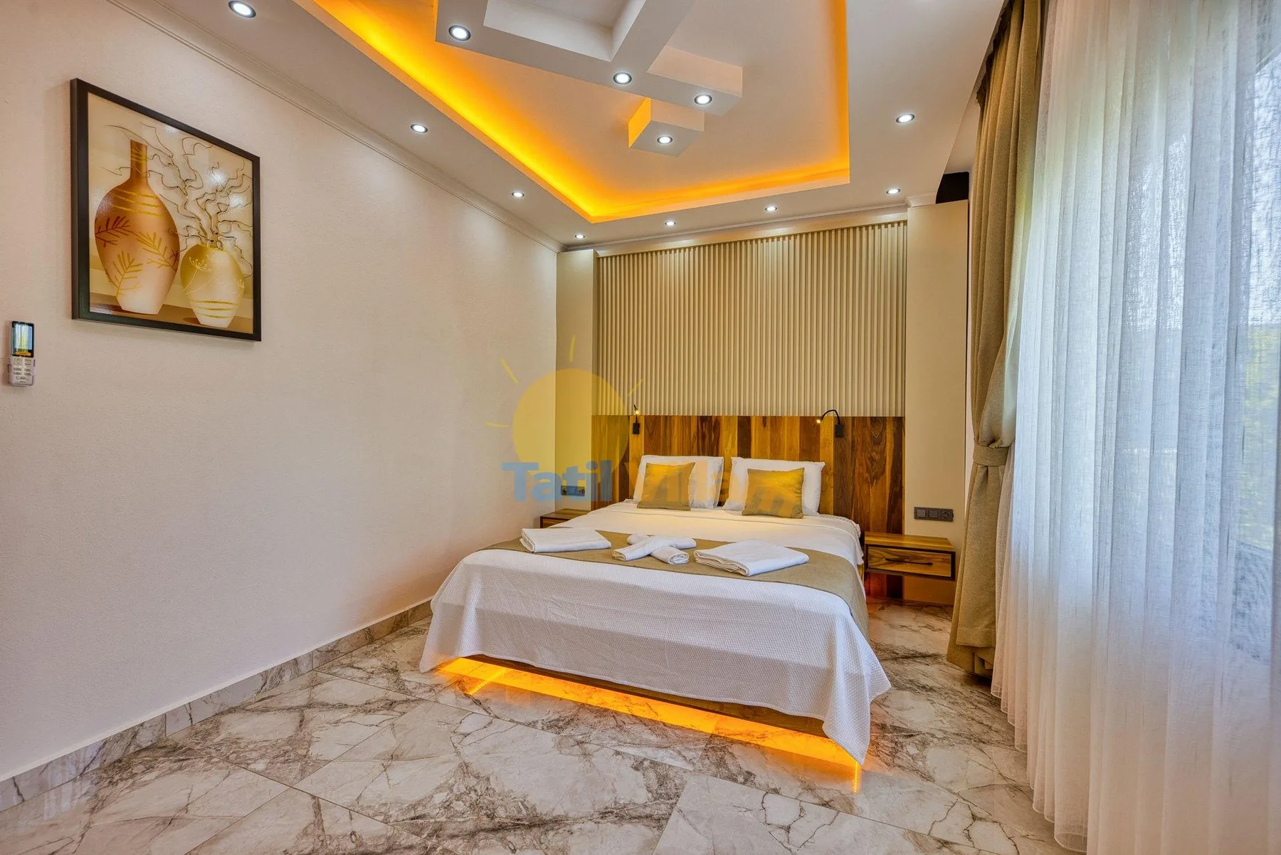 A bedroom with a neatly made bed, bedside tables, and floor-length curtains.