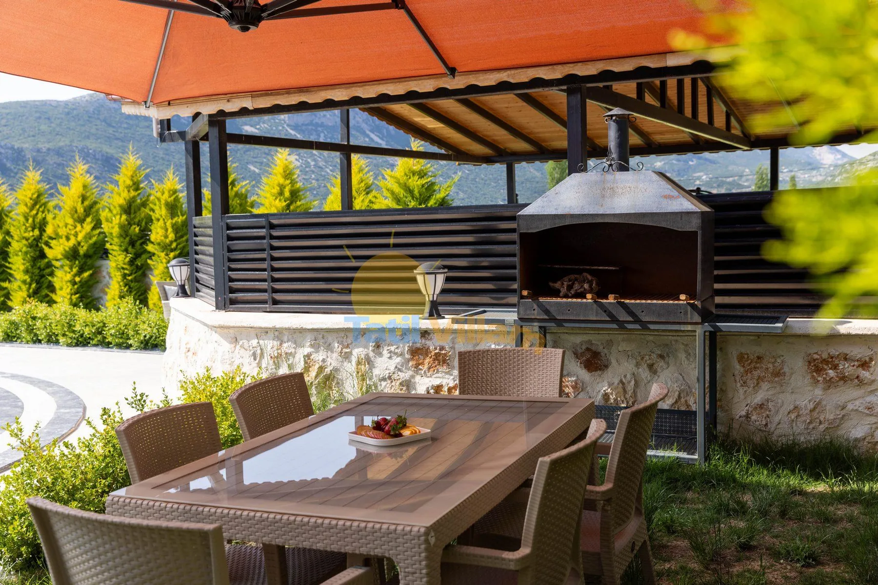 An outdoor dining area under an orange umbrella, with a built-in grill nearby.