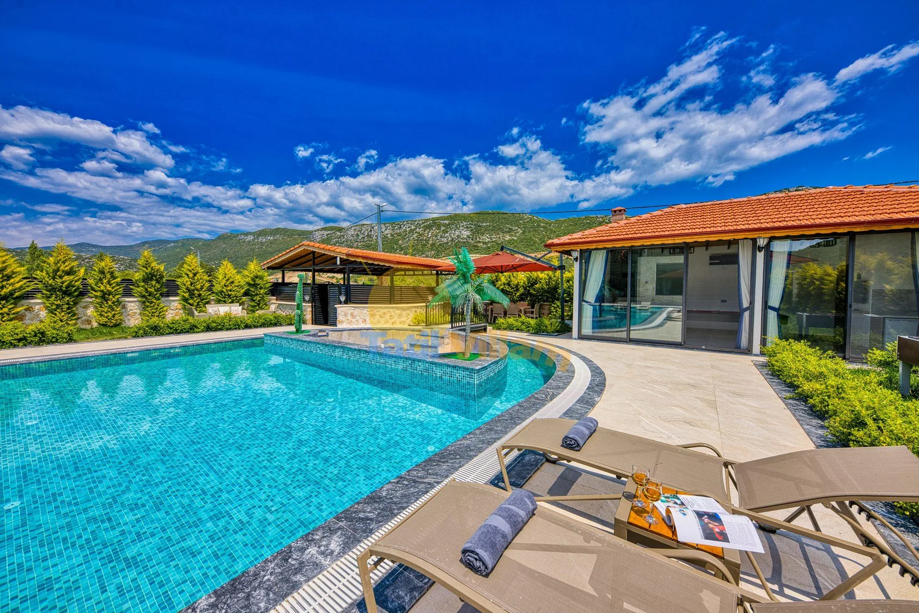 An outdoor pool beside a paved patio and a building with a red tile roof.