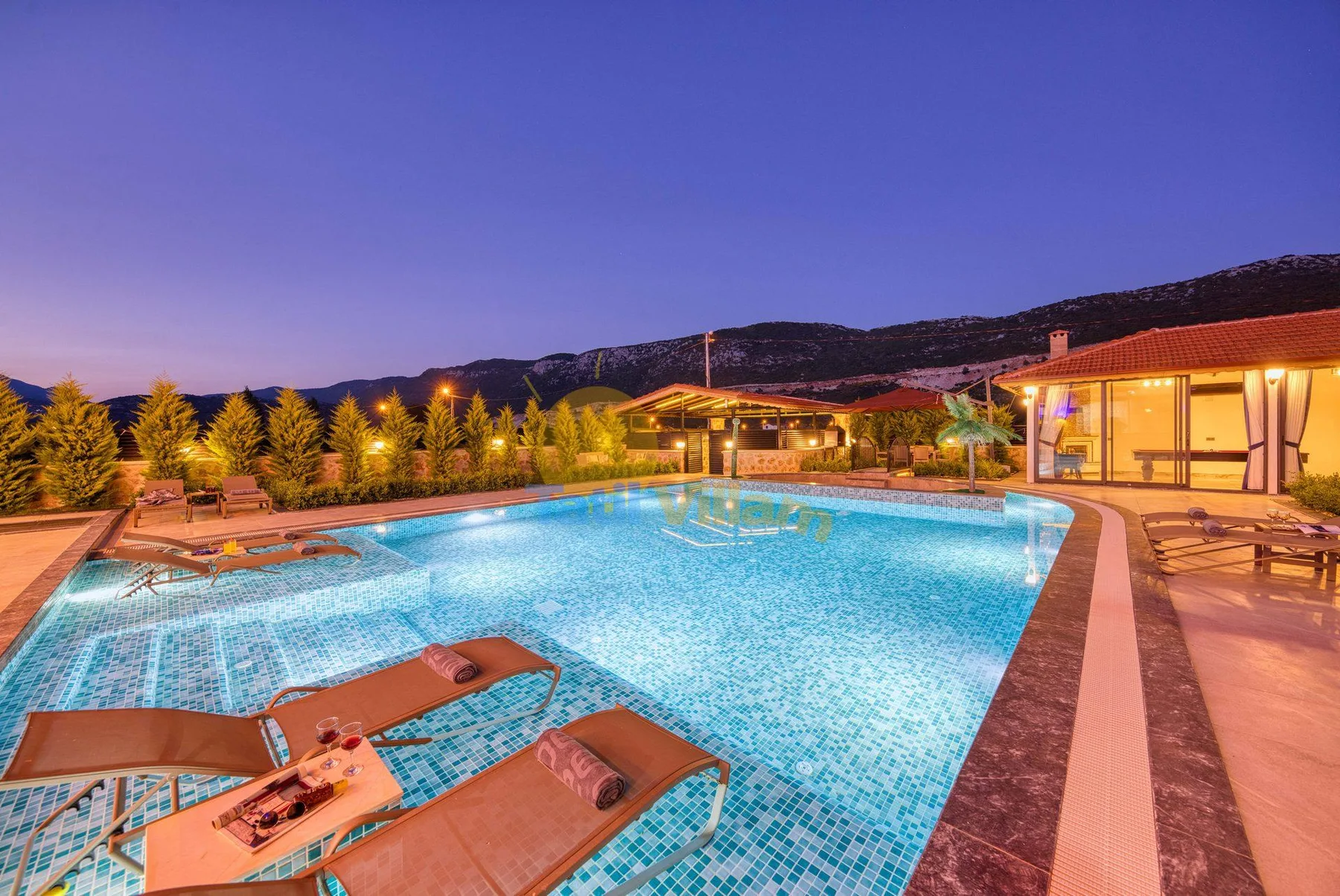 An outdoor swimming pool glows at dusk beside a lit building.