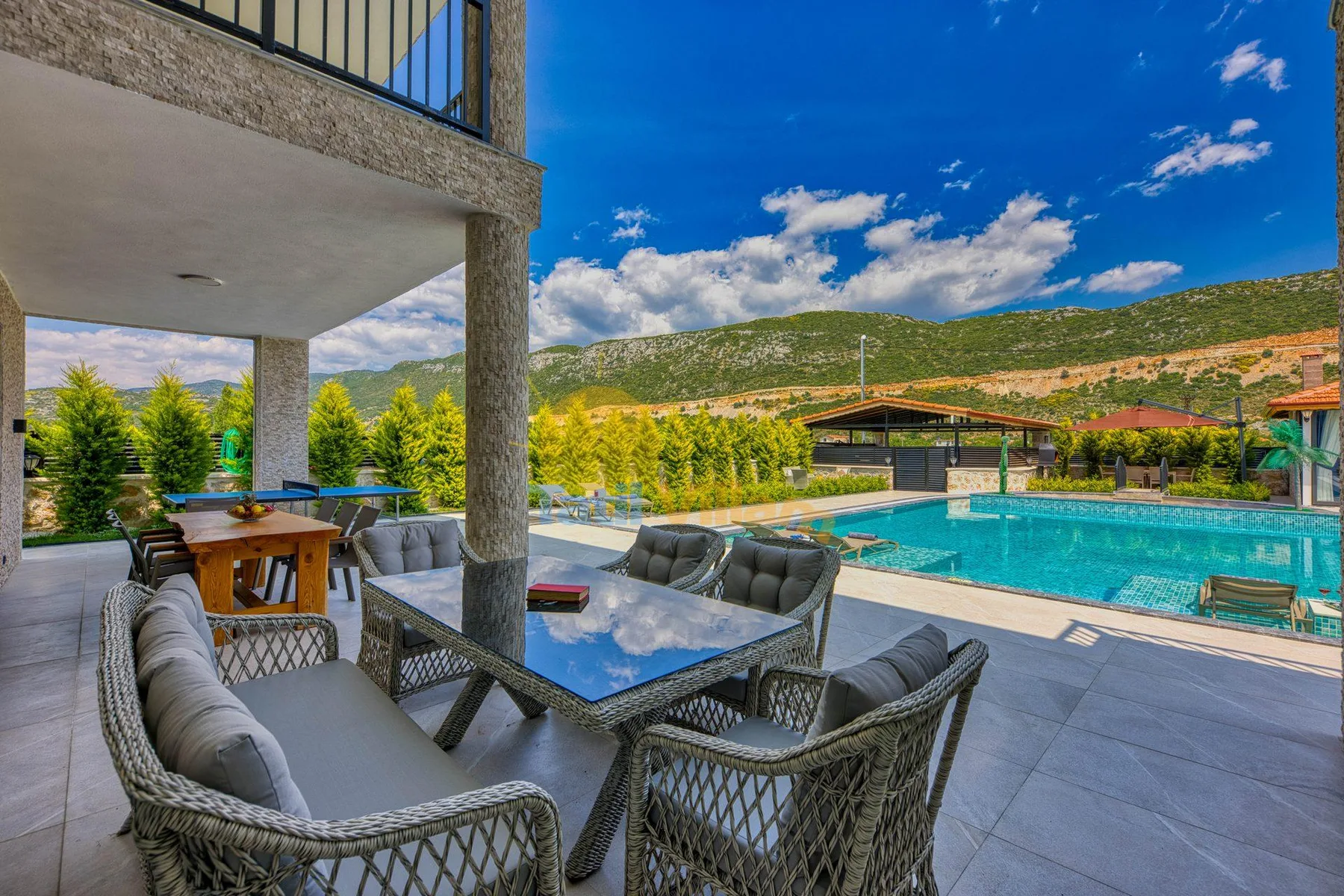 An outdoor dining and seating area overlooks a swimming pool and mountain landscape.